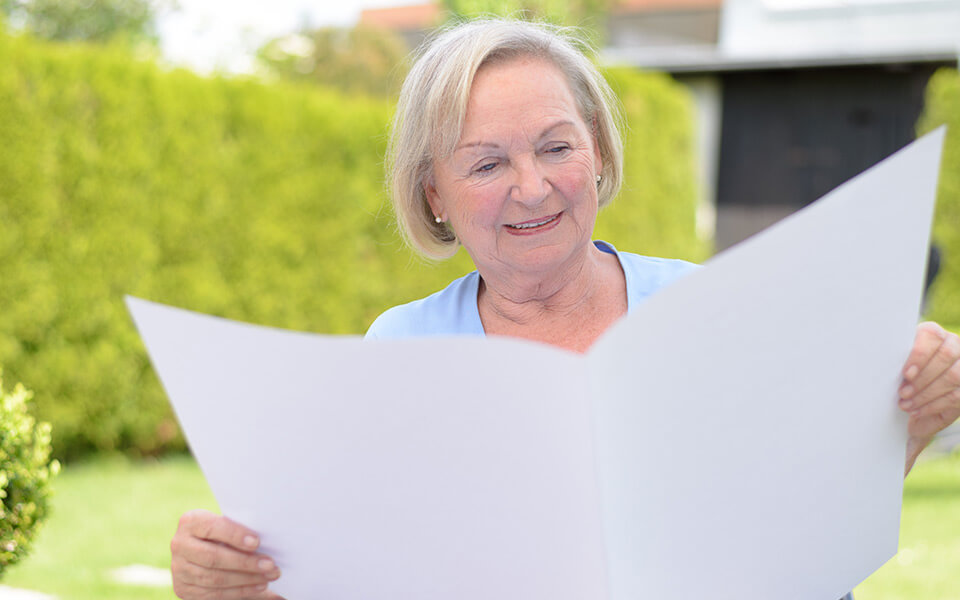 Elderly woman reading a large document outside